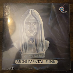 May include: A vinyl record album cover featuring a blue-toned illustration of a person with long hair depicted as a stone bust. The text reads Mark Farner and Monumental Funk. A small circular logo with a colorful spiral is in the top right corner.