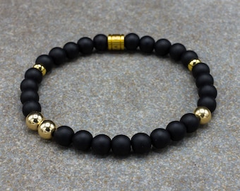 Puede incluir: Un brazalete de cuentas mate negras con detalles dorados. El brazalete tiene un diseño sencillo y está hecho con materiales de alta calidad.