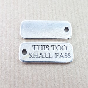 May include: Two silver metal tags. The top tag is blank. The bottom tag has the text "This too shall pass" engraved on it.