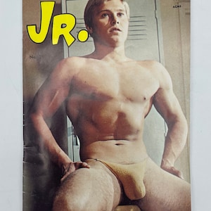 May include: Magazine cover with a shirtless man in a yellow thong. The title "JR." is in yellow. The text at the top reads "The Strength of America Lies in Its Youth." The bottom text says "The Boy's Guide to Physical Fitness."