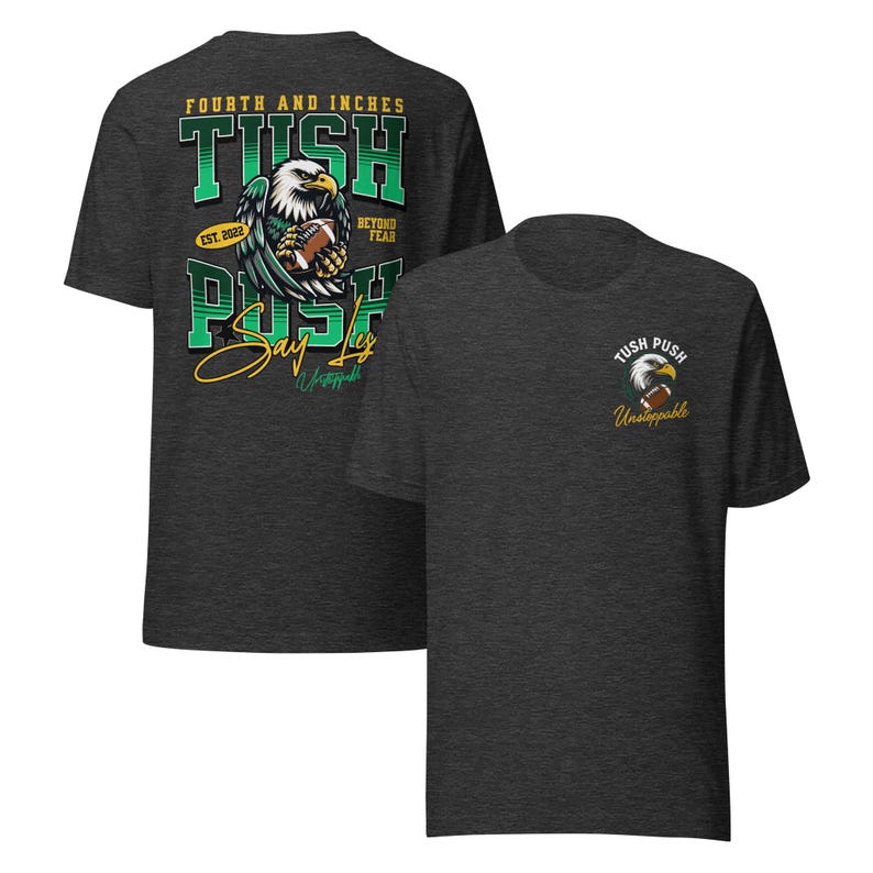 May include: Dark grey t-shirts with a football theme. One shirt features a large graphic of an eagle holding a football, with the text "FOURTH AND INCHES TUSH PUSH Say Less" and "EST. 2022". The other shirt has a smaller eagle graphic and the text "TUSH PUSH Unstoppable".