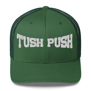 May include: A forest green trucker hat featuring a structured front panel and a breathable mesh back. The front of the cap displays the text TUSH PUSH embroidered in bold, white, block-style capital letters across the center of the crown.