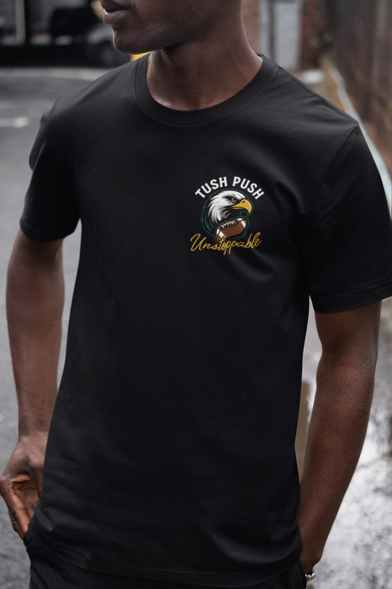 May include: Black t-shirt with an eagle head and football graphic, and the words "Tush Push Unstoppable" in white and gold. The shirt is made of a soft, comfortable material.