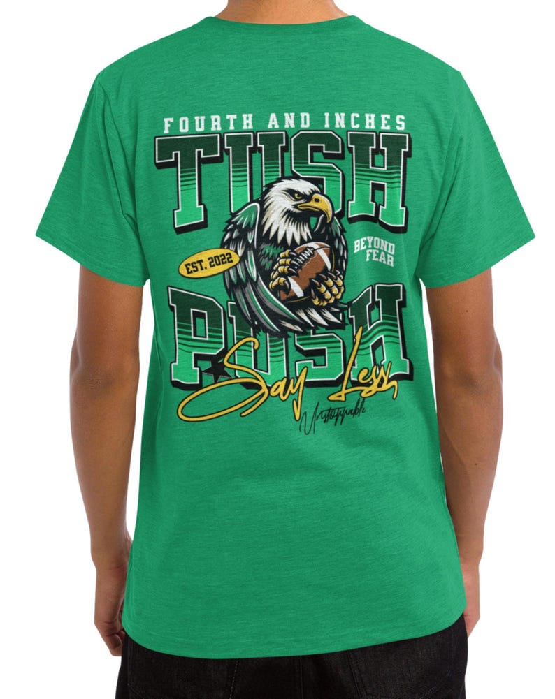 May include: Green t-shirt with a graphic design featuring an eagle clutching a football. The text on the shirt reads "FOURTH AND INCHES TUSH PUSH" with "EST. 2022" and "BEYOND FEAR" included. The shirt also has the words "Say Less" and "Unstoppable".