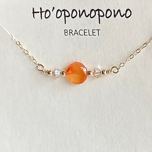 May include: A gold chain bracelet with a small orange gemstone and clear crystal beads. The bracelet card reads "Ho'oponopono Bracelet" and "I'm sorry. Forgive me. Thank you. I love you."