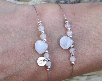 Puede incluir: Dos delicados brazaletes de plata con cuentas de piedra lunar y un dije de plata. Los brazaletes están en la muñeca de una persona.