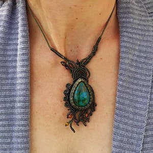 May include: A green gemstone pendant necklace with a knotted cord and small beads. The pendant is a teardrop shape with a dark green and blue color.