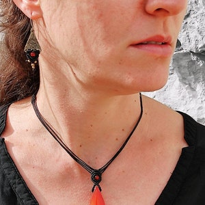 May include: A black cord necklace with a red and orange agate pendant. The pendant is shaped like a teardrop and has a smooth, polished finish.