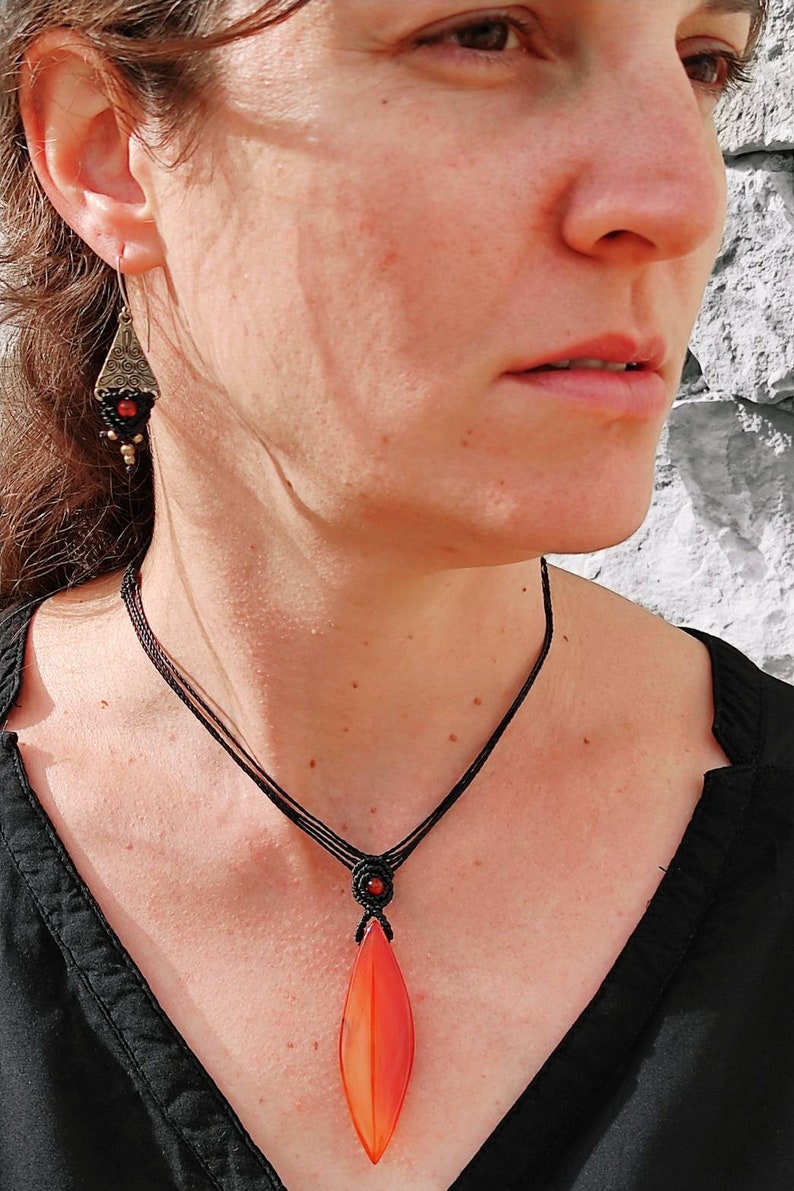 May include: A black cord necklace with a red and orange agate pendant. The pendant is shaped like a teardrop and has a smooth, polished finish.