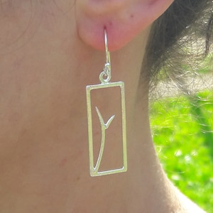 Puede incluir: Pendientes de plata con forma rectangular y un delicado diseño de rama en su interior.