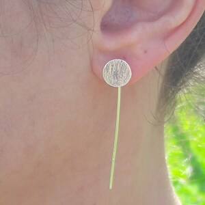 May include: Silver dangle earrings with a textured round disc and a long, thin silver post.