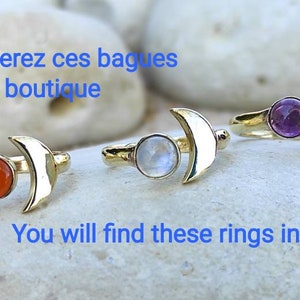 May include: Four gold crescent moon rings with different colored gemstones. The rings feature a crescent moon design with a gemstone set in the center. The gemstones are orange, white, purple, and a light blue color.