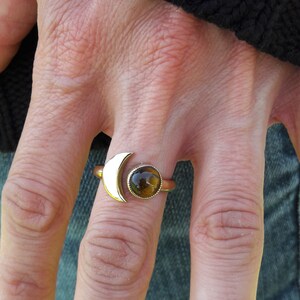 May include: Gold ring with a crescent moon design and a round tiger's eye gemstone.
