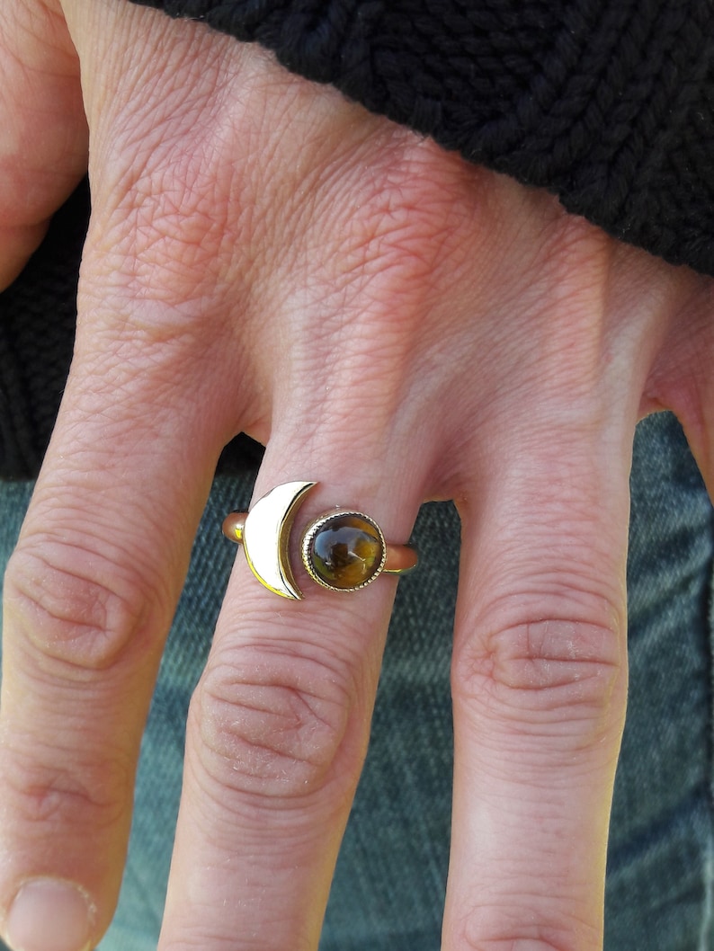 May include: Gold ring with a crescent moon design and a round tiger's eye gemstone.