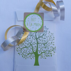 May include: A white envelope with a green tree design and a brown sticker that says "FAIT &Agrave; LA MAIN". The envelope is tied with a gold and silver ribbon.