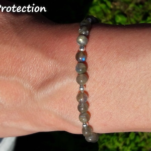 May include: A gray beaded bracelet with silver accents. The bracelet is on a person's wrist. The text "Protection" is visible in the top left corner of the image.