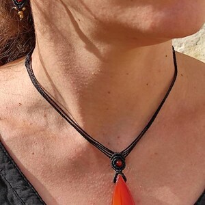 May include: A black cord necklace with a red carnelian pendant in the shape of a leaf. The pendant is polished and has a red, orange, and yellow color gradient.