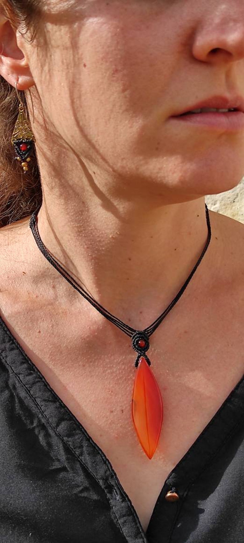 May include: A black cord necklace with a red carnelian pendant in the shape of a leaf. The pendant is polished and has a red, orange, and yellow color gradient.