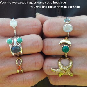 May include: A set of silver rings with turquoise and moonstone gemstones. The rings are stacked on two fingers. The rings are on a hand with a gold ring with a starfish design on the other finger.
