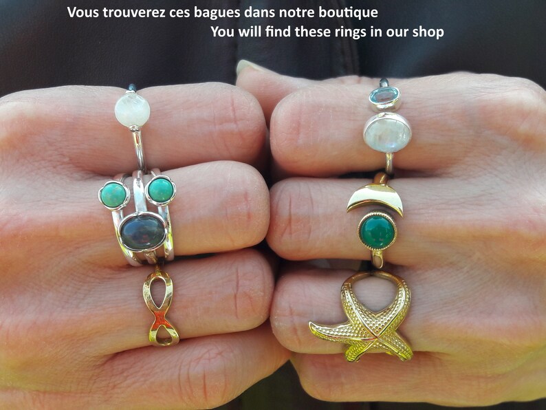 May include: A set of silver rings with turquoise and moonstone gemstones. The rings are stacked on two fingers. The rings are on a hand with a gold ring with a starfish design on the other finger.