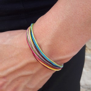 Peut inclure: Un bracelet tressé coloré avec plusieurs brins de fil dans des tons de rouge, jaune, bleu, vert et marron.