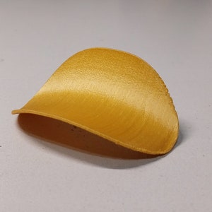 May include: A golden yellow, 3D printed, plastic, leaf-shaped object.