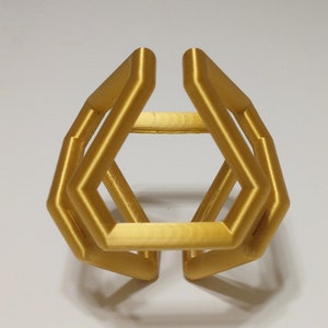 May include: A gold-colored, geometric, 3D printed ring with a hexagonal shape.