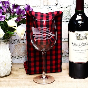 May include: A clear wine glass with an etched American flag design. The glass is sitting on a red and black checkered cloth.