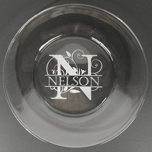 May include: A clear glass plate with a silver etched design of the letter N with a floral pattern and the name "NELSON" below it.