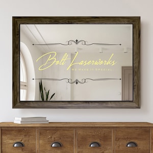 May include: A brown wooden framed mirror with a yellow inscription that reads "Bolt Laserworks, We Make It Special" with decorative flourishes above and below the text.