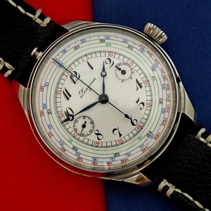 Könnte beinhalten: Eine vintage Longines Chronograph-Armbanduhr mit weißem Zifferblatt, schwarzen Zeigern und einem schwarzen Lederarmband. Die Uhr hat eine mehrfarbige Tachymeterskala am äußeren Rand des Zifferblatts.