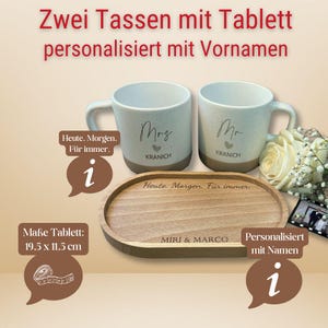 May include: Two speckled ceramic mugs, one labeled "Mrs" and the other "Mr", with the last name "KRANICH" below. They sit on a wooden tray, 19.5 x 11.5 cm, engraved with "MIRI & MARCO" and "Heute Morgen. F&uuml;r immer."