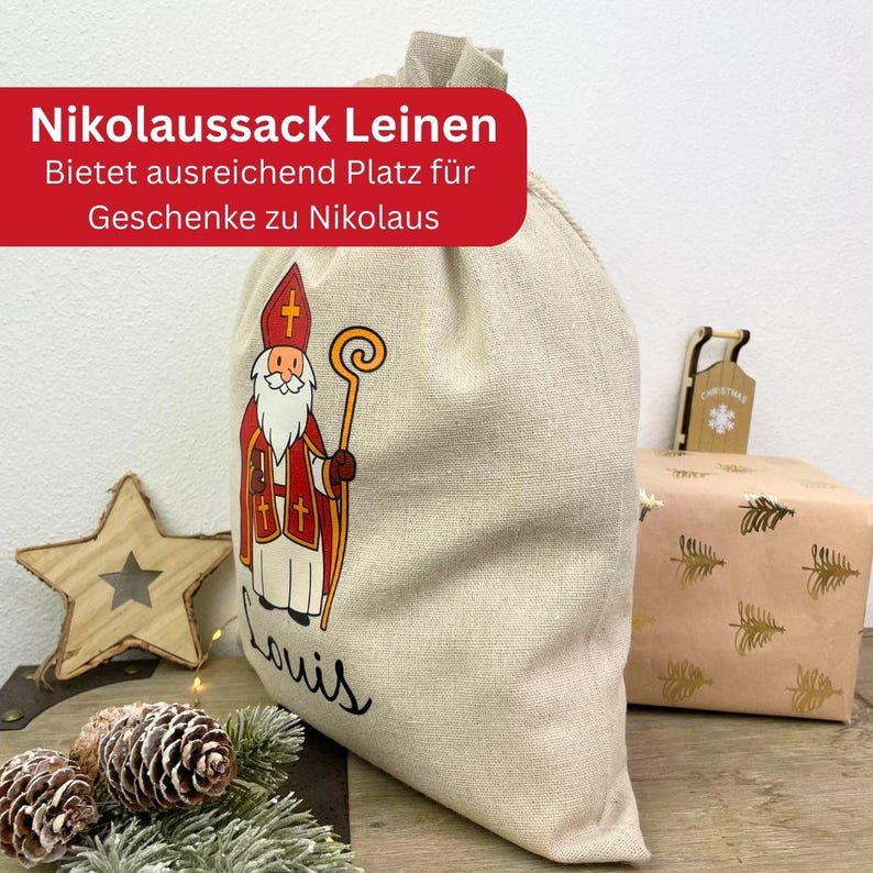 May include: A beige linen gift bag with a drawing of Santa Claus in red and white, holding a gold staff. The bag has the name "Louis" written in black script. A red banner at the top reads "Nikolaussack Leinen".