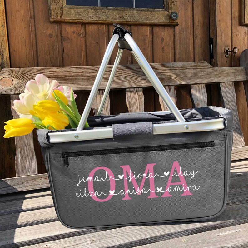 May include: Gray canvas tote bag with a zipper closure and two silver handles. The bag has pink lettering that says "OMA" with the names "jamail, fiona, ilay, eliza, anisa, amira" written underneath in a smaller font.