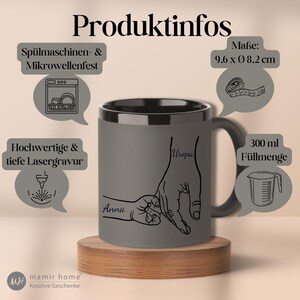 Op de afbeelding: Grijze keramische mok met een zwarte binnenkant en handvat, met een lijntekening van twee handen die elkaar vasthouden. De mok is 9,6 cm x 8,2 cm en bevat 300 ml. De namen "Anna" en "Uropa" staan op de mok.