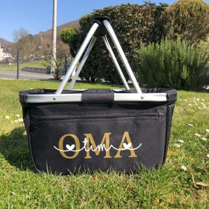 May include: Black canvas tote bag with a silver metal frame and handles. The bag has a zippered pocket and the word "OMA" written in gold with two white hearts.