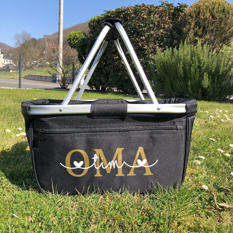 May include: Black canvas tote bag with a silver metal frame and handles. The bag has a zippered pocket and the word "OMA" written in gold with two white hearts.