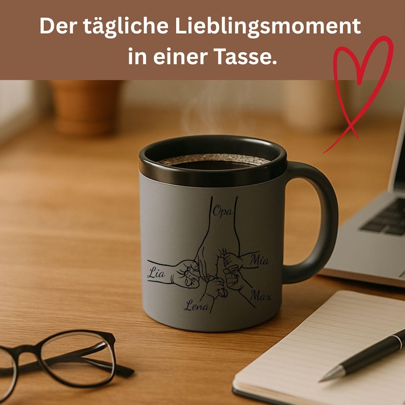 Op de afbeelding: Een grijze keramische mok met een zwarte rand en handvat, gevuld met koffie. De mok heeft een familiehand-ontwerp met namen: Opa, Mia, Max, Lena en Lia. Bovenstaande tekst luidt: "Der t&auml;gliche Lieblingsmoment in einer Tasse."