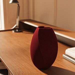 Peut inclure: Un vase en céramique rouge avec une ouverture en forme de cœur unique et une texture côtelée posé sur un bureau en bois.