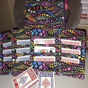 Peut inclure: Ensemble de porte-cartes avec un motif abstrait coloré. Les porte-cartes noirs présentent un motif de formes et de lignes arc-en-ciel. Deux jeux de cartes Maverick sont devant, avec du texte en anglais et en français.