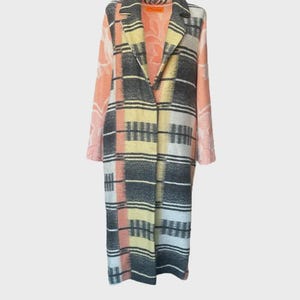 May include: A long, open-front coat with a striking geometric pattern. The coat features a mix of colors, including gray, yellow, pink, and white, arranged in a plaid design. The sleeves have a floral pattern. The coat is a stylish outerwear piece.