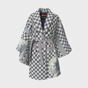 Op de afbeelding: Een grijs en wit geruite kimono-achtige badjas met bijpassende riem. De badjas heeft een portret op de mouwen en een gestreept patroon op de randen. De badjas is gemaakt van een zachte, vloeiende stof.