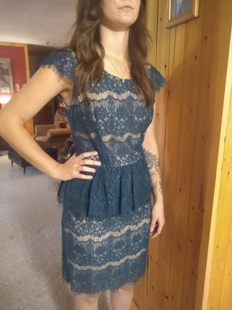 Puede incluir: Un vestido de encaje azul turquesa con falda con volantes y corpi&ntilde;o ajustado. El vestido tiene un escote festoneado y mangas cortas.