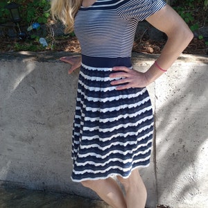 May include: A navy and white striped dress with a scoop neckline and short sleeves. The bodice has horizontal stripes, and the skirt has a scalloped hem. A navy band defines the waist. The dress is knee-length.