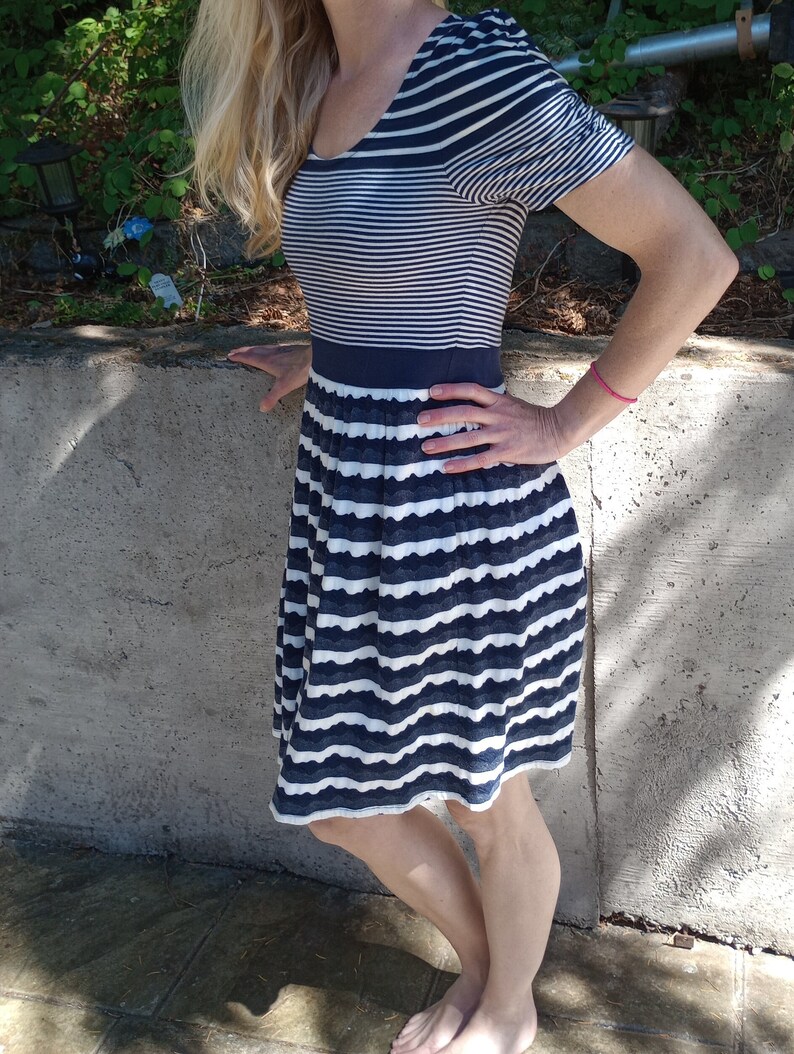 May include: A navy and white striped dress with a scoop neckline and short sleeves. The bodice has horizontal stripes, and the skirt has a scalloped hem. A navy band defines the waist. The dress is knee-length.