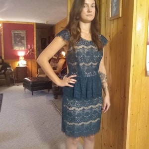 Puede incluir: Un vestido de encaje azul verdoso con un corpi&ntilde;o ajustado y una falda acampanada. El vestido tiene un dobladillo festoneado y un escote redondo.