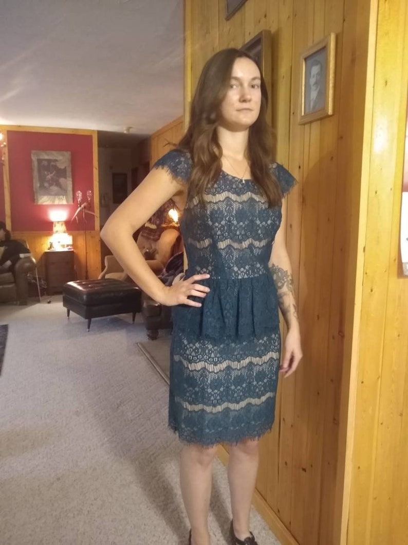 Puede incluir: Un vestido de encaje azul verdoso con un corpi&ntilde;o ajustado y una falda acampanada. El vestido tiene un dobladillo festoneado y un escote redondo.