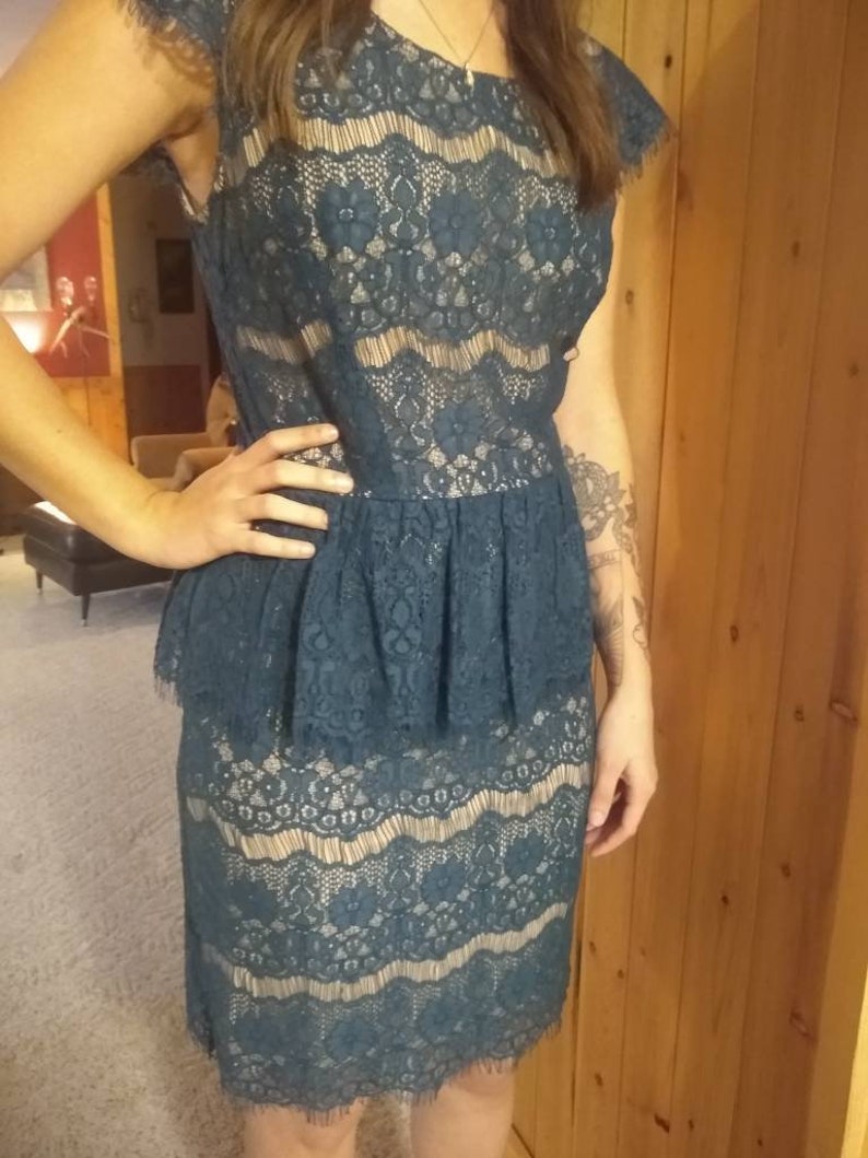 Puede incluir: Un vestido de encaje azul turquesa con una falda con volantes y un corpi&ntilde;o ajustado. El vestido tiene un delicado estampado floral y un dobladillo festoneado.