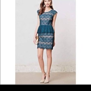 Puede incluir: Un vestido de encaje azul turquesa con cintura peplum y mangas cortas. El vestido es entallado y tiene un dobladillo festoneado.
