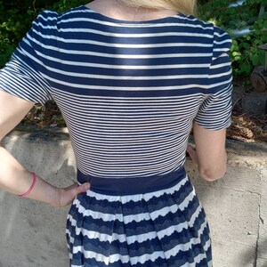 May include: A navy and white striped dress. The top has short sleeves and a scoop neckline. The skirt is pleated with a scalloped edge. The dress is fitted at the waist.